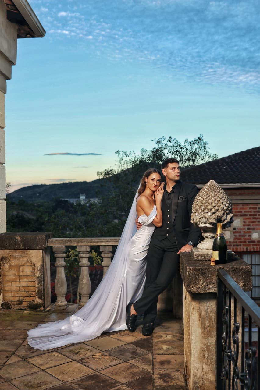A couple on a stone terrace at dusk, the bride's train spread across tiled paving.