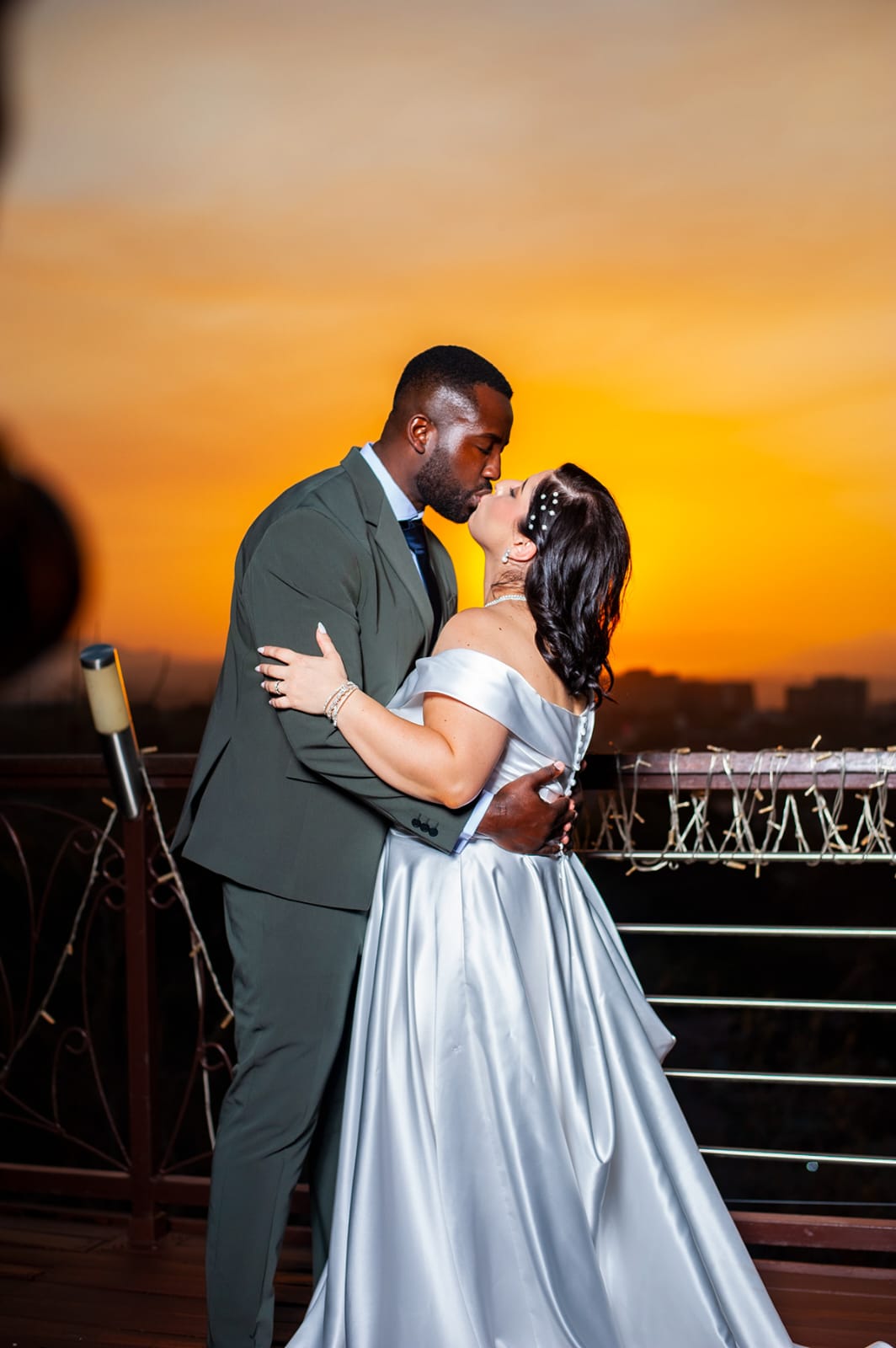 A couple kissing on a balcony against a deep amber sunset.